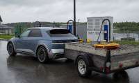 Hyundai Ioniq 5 towing a utility trailer while parked near EV charging stations on a rainy day.