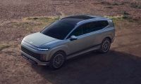 Aerial three-quarter view of a Hyundai IONIQ 9 electric SUV with a sleek gray exterior on a dirt overlook.