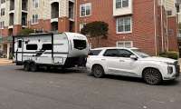 White Hyundai Palisade towing a Flagstaff Micro Lite travel trailer on a residential street.