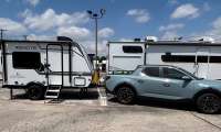 Light blue Hyundai SUV towing a white Coachmen Remote travel trailer at an RV dealership lot