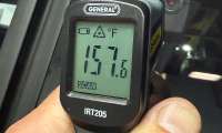 Infrared thermometer showing a 157.6-degree Fahrenheit temperature reading inside a vehicle.