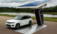 White Jeep Grand Cherokee 4xe plugged into a Jeep-branded charging station with a large solar canopy.