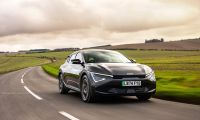 Kia EV6 electric crossover driving along a scenic rural highway under dramatic cloudy skies.
