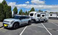 Kia EV9 towing a small travel trailer while parked at an EV charging station