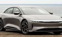 Silver Lucid Air electric sedan parked on a dirt bluff overlooking the ocean, front three-quarter view showing signature light bar headlights