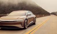 Image of a gold Lucid Air driving on a mountain road.