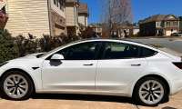 Marcio Cavalcanti's former white Tesla Model 3 shown in a full side profile while parked in a residential driveway, the EV he owned before switching to his current Ford Mustang Mach-E.