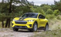 Bright yellow Ford Mustang Mach-E Rally driving on dirt trail through forest