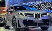 New BMW iX3 electric SUV in gray on display at auto show with illuminated kidney grille and blue light backdrop