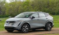 Gray Nissan Ariya parked on a gravel path beside green fields and trees.