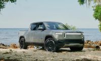 Rivian R1T parked on sandy beach with coastal trees