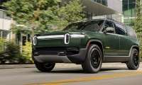 Green Rivian R1S electric SUV shown from a low front angle while driving in an urban setting.