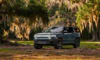 Gray-blue Rivian R1S SUV parked under oak trees draped in Spanish moss, front three-quarter view