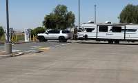 White Rivian R1S and Passport travel trailer shown in side profile at an EV charging station.