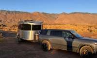 Rivian R1S towing an Airstream trailer at a desert campsite with mountains in the background.
