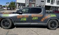 Gray Rivian R1T parked on a city street with “don’t buy junk” graffiti painted on the side.