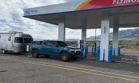 Blue Rivian R1T towing an Airstream travel trailer at a GM Energy Flying J charging station.
