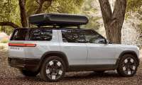 White Rivian R2 parked under trees with a rooftop cargo box in a side-profile view.