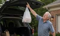 A man winces in pain as he reaches up to tap a tailgate close button