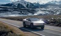 Tesla Cybertruck driving on a mountain road with snow-capped peaks in the background