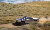 Tesla Cybertruck driving fast on a dusty off-road trail through rolling hills under a cloudy sky.