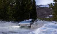 Tesla Cybertruck driving through a snowy water crossing and throwing up a large splash in a winter forest.