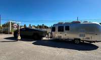 Tesla Cybertruck towing an Airstream travel trailer in a parking lot with a person standing beside the truck.