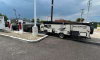 Tesla Cybertruck towing a Rockwood travel trailer while parked at a Tesla Supercharger station