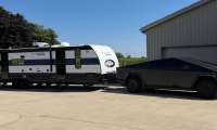 Tesla Cybertruck hitched to a large travel trailer outside a garage on a sunny day.
