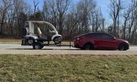 Red Tesla Model Y towing a trailer with a golf cart, electric SUV hauling in parking lot