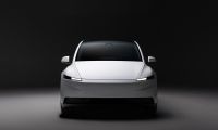 White Tesla Model Y front view in a dark studio setting, highlighting minimalist design and LED headlights