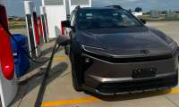 Dark gray Toyota bZ electric SUV connected to a Tesla Supercharger at a highway charging station.