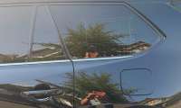Close-up of a black Toyota Grand Highlander’s rear passenger window, door, and fuel door reflecting nearby homes and the photographer.