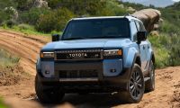 2026 Toyota Land Cruiser heritage blue driving on dirt trail through rocky mountain terrain