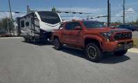Toyota Tacoma towing an Outback travel trailer in a front three-quarter view near an intersection.