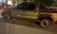 Bronze Oxide Toyota Tacoma Trailhunter parked at night on a city street in side profile.