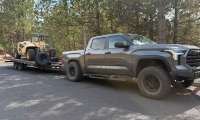 Side view of a Toyota Tundra towing a flatbed trailer with a Gehl telehandler.