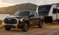 Dark brown Toyota Tundra towing a black and white Brinkley travel trailer beside a lake at sunset