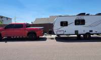 Red Toyota Tundra towing a Coachmen Apex camper trailer in a full side view on a residential street.