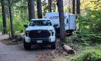 Toyota Tundra towing a Coleman travel trailer at a wooded campsite.