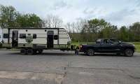 Black Toyota Tundra towing a Forest River NOBO travel trailer on a residential street while a person checks the hitch area.