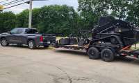 Gray Toyota Tundra towing a large equipment trailer with a black skid steer loaded on it.