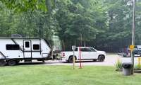 White Toyota Tundra pickup towing a white travel trailer at a wooded campground