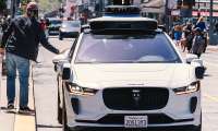 Waymo Jaguar I-Pace robotaxi stopped on a busy city street as a pedestrian passes beside it.
