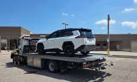 White Toyota Rav 4 being loaded onto a flatbed tow truck in a parking lot