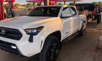 White Toyota Tacoma refueling at a Maverik gas station while towing a black utility trailer.