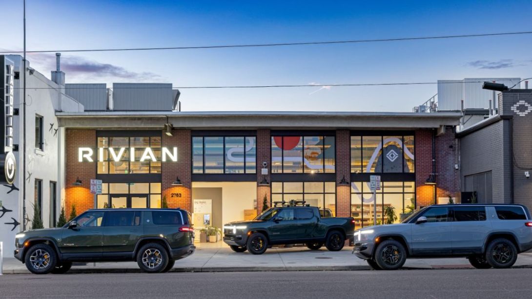 Rivian R1T and R1S electric vehicles parked outside a Rivian showroom at dusk.
