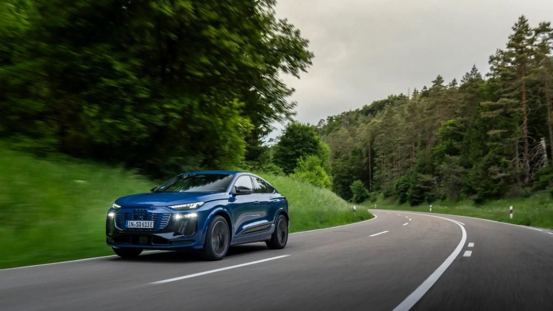 Blue Audi Q4 e-tron electric SUV driving on a winding forest highway in motion