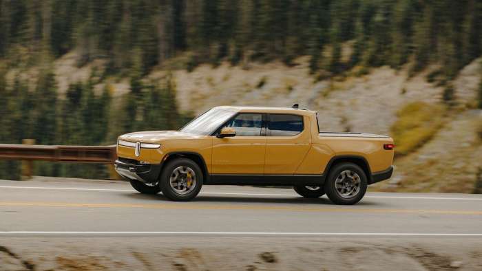 A yellow Rivian R1T is pictured driving on a mountain road.