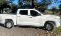 2025 Toyota Tundra, Front 3_4 Quarters, White 2025 Toyota Tundra crew cab pickup in white, photographed from passenger side, featuring chrome wheels and running boards, parked outside residential home.